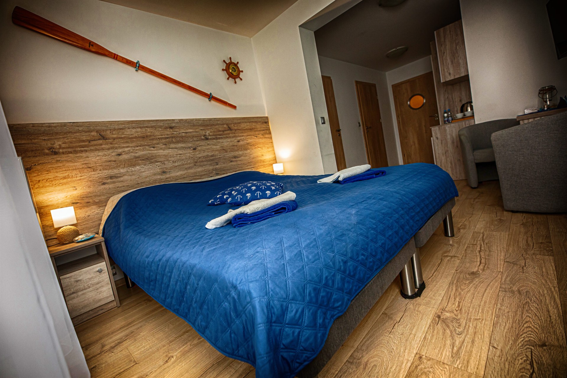 Duże łóżko z granatową narzutą, poduszką z kotwicami, złożonymi ręcznikami i wiosłem na ścianie