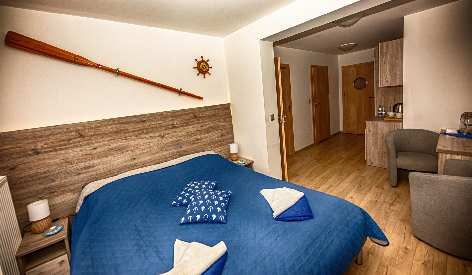 Sypialnia z niebieską narzutą, drewnianym wiosłem na ścianie i poduszkami z kotwicami