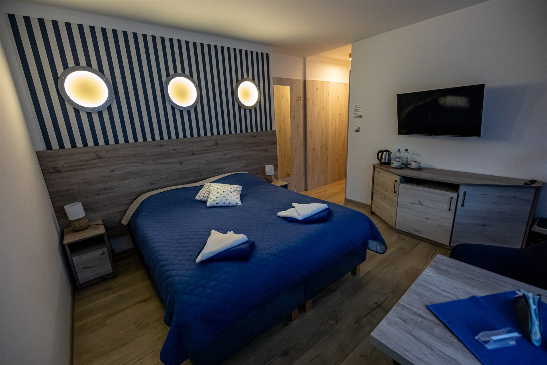 Pokój hotelowy z łóżkiem w granatowej narzucie i trzema okrągłymi świetlami na pasiastej ścianie