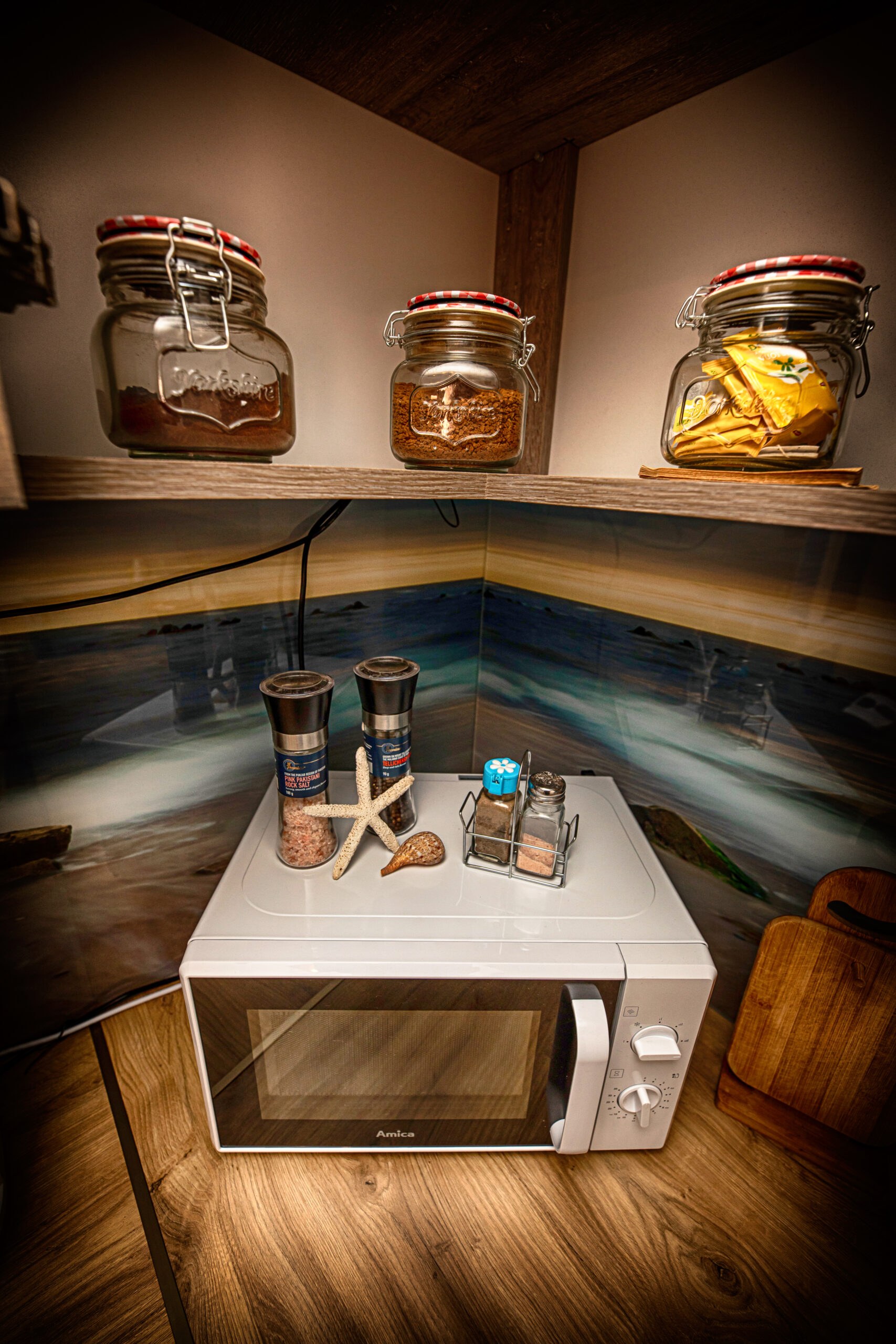 Biała mikrofalówka na drewnianym blacie z młynkami soli i pieprzu, rozgwiazdą i słoikami na półce