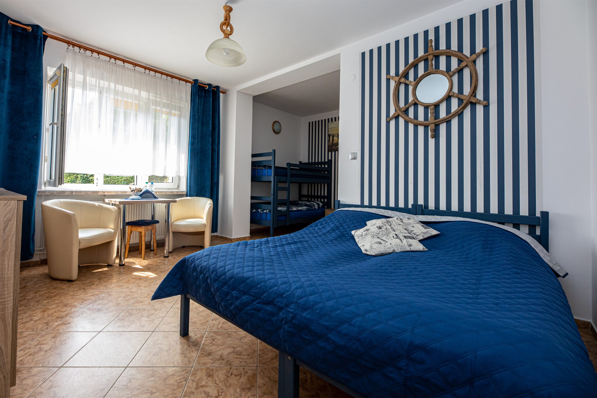 Sypialnia marynistyczna z granatowym łóżkiem, pionowymi biało-granatowymi pasami i drewnianym kołem sterowym